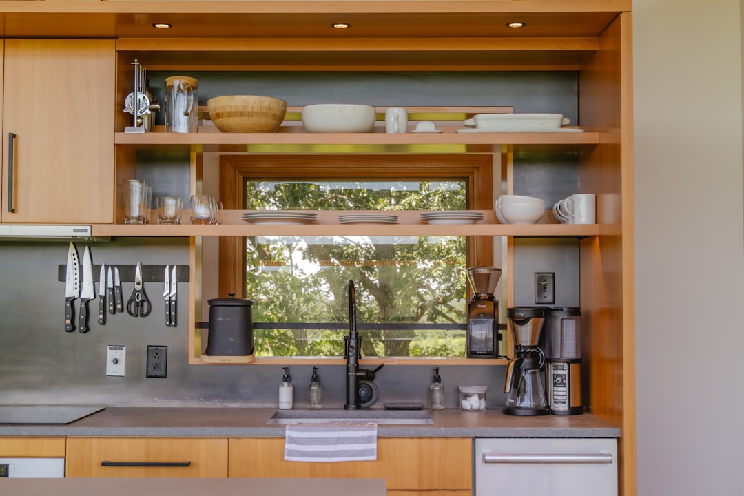 A clean countertop with a kettle and milk frother beside two mugs and cocoa tools