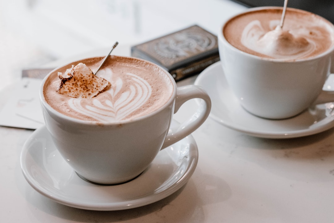 Milk frother on countertop with a cappuccino mug and cocoa mug for both morning and evening drinks